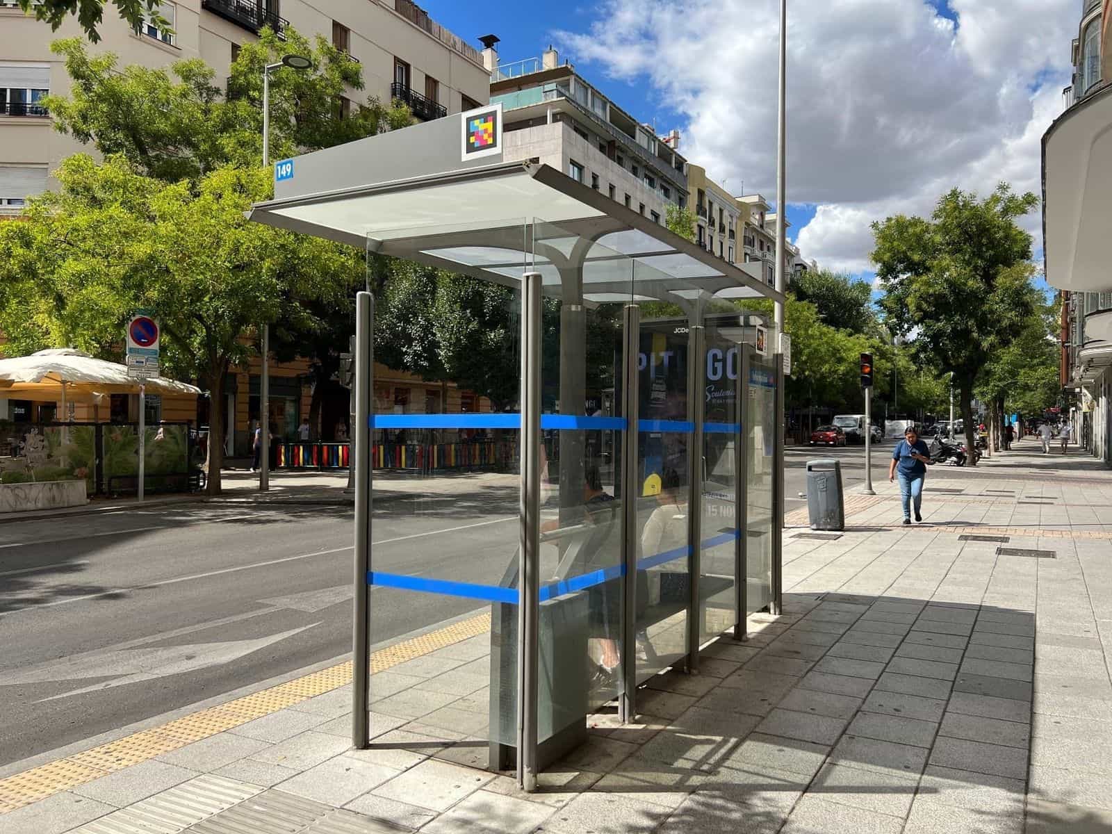 Pensilina in vetro della EMT in strada, con la targa numerica «149» in blu; sul frontale del tetto un codice NaviLens quadrato a colori risalta su fondo bianco perché l’app del telefono lo rilevi dal marciapiede opposto