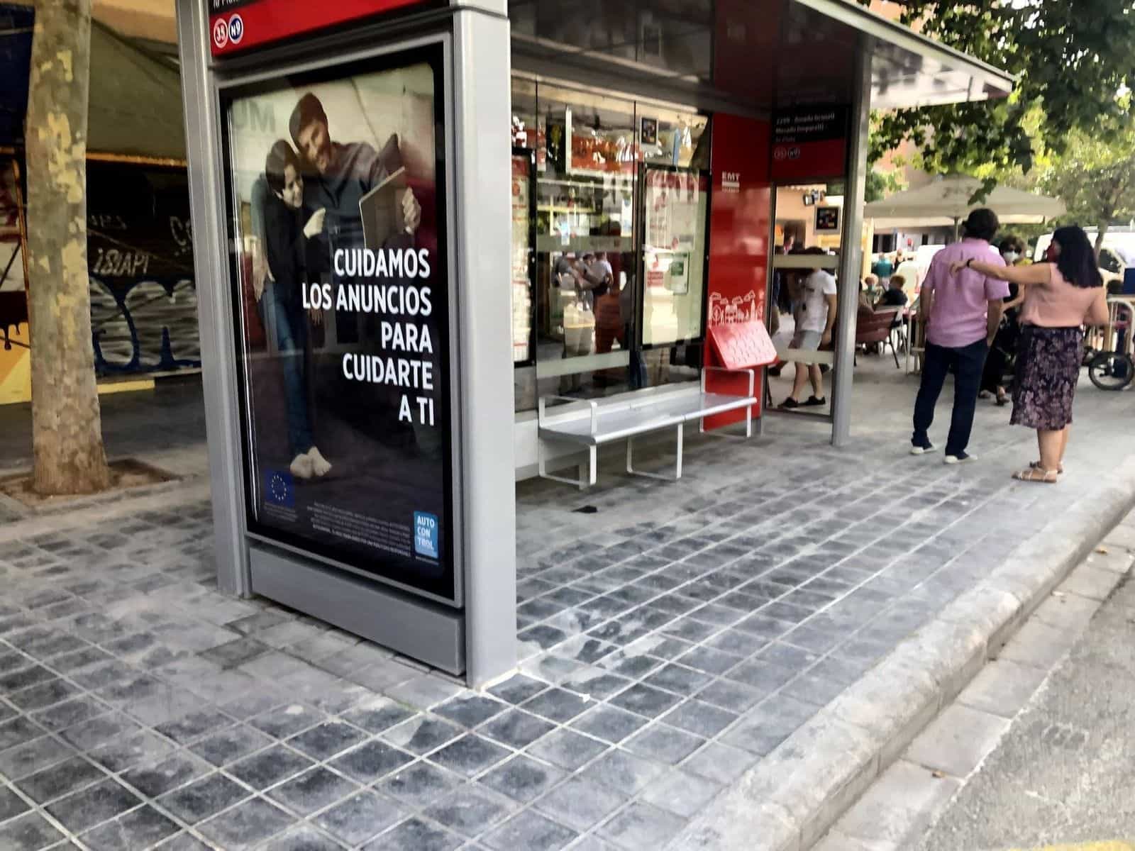 Pensilina della EMT València vista dal marciapiede, con un MUPI pubblicitario «Cuidamos los anuncios para cuidarte a ti» di Autocontrol e, sulla testata rossa, la targa numerica della fermata con un codice NaviLens accanto al testo «Escaneja amb»