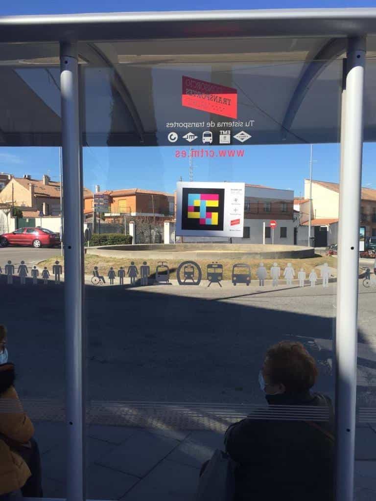 “Scan with” sign with a colour NaviLens code, NaviLens and NaviLens GO app icons, CRTM logo and Clear Channel logo stuck on a shelter’s glass