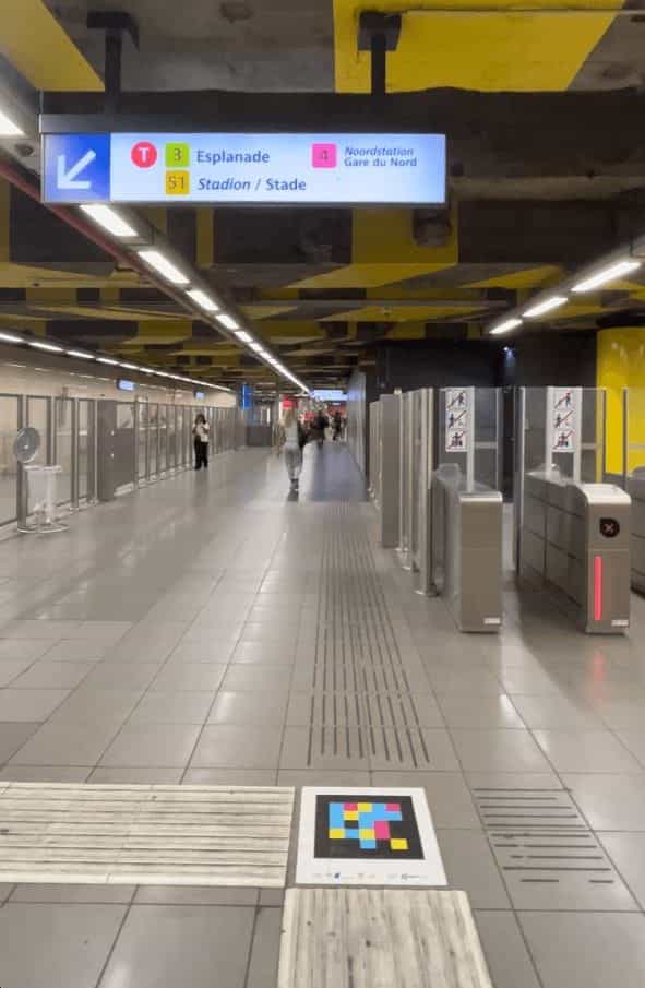Brussels metro concourse with platform direction sign and NaviLens code on the tactile strip
