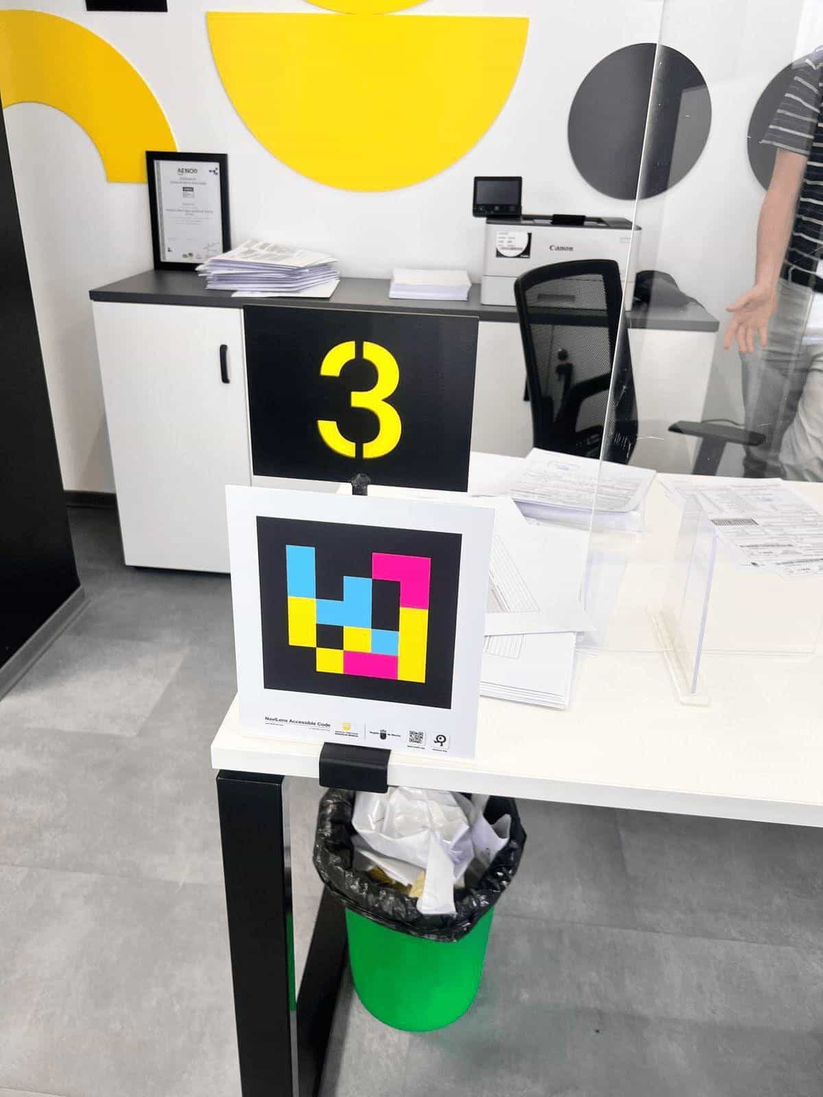 Puesto de atención número 3 dentro de la oficina ATRM de Fortuna: cabecera negra con un gran «3» en amarillo retroiluminado, mampara transparente, mostrador blanco y panel cuadrado con código NaviLens.