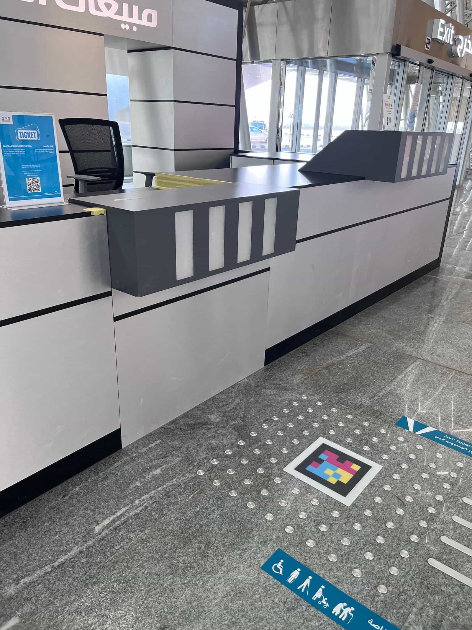 「Ticket — cancellations & modifications」と表示されたSARの券売カウンター。床には「mobility only」ピクトグラムの隣にNaviLensコード