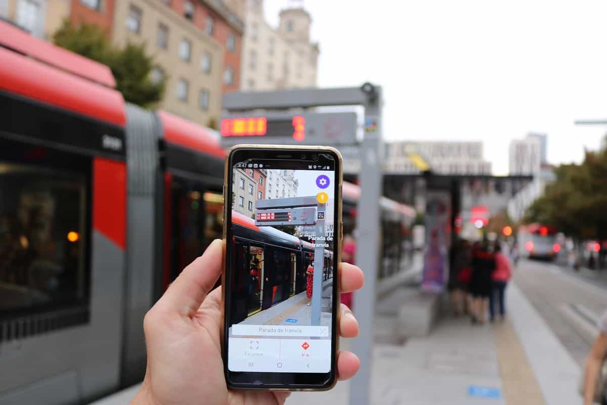 Móvil mostrando la app NaviLens leyendo la parada del tranvía de Zaragoza con un Urbos rojo al fondo