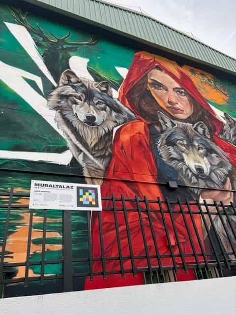Detalle del mural «Familia de lobos» de Asem Navarro con placa blanca «MURALTALAZ» y código NaviLens cuadrado a colores.
