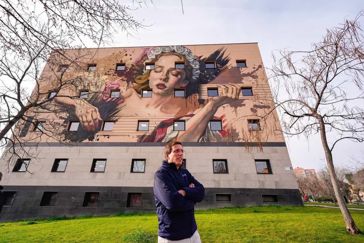 Mural de SFHIR sobre la fachada de un edificio municipal de Moratalaz: mujer joven con corona de rosas blancas sobre fondo arena, ocupando seis plantas.