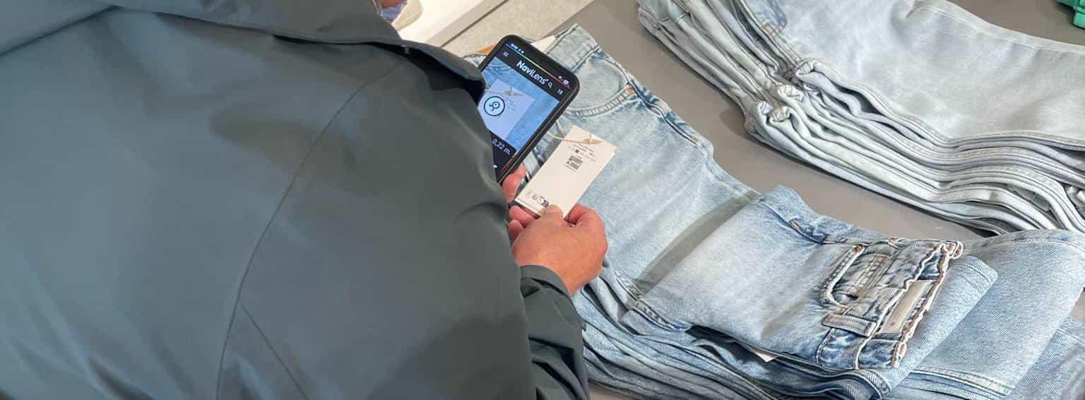 Customer scanning a NaviLens hangtag on a pair of jeans with a smartphone in a fashion store.