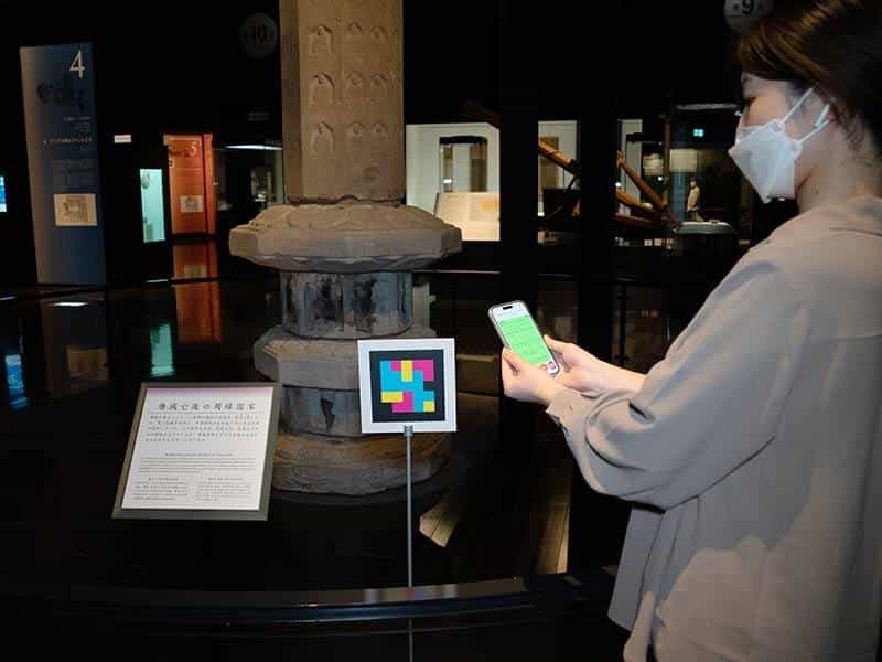 A visitor scans the NaviLens code installed next to a stone stupa and its label with her smartphone, in the Cultural Exchange Exhibition