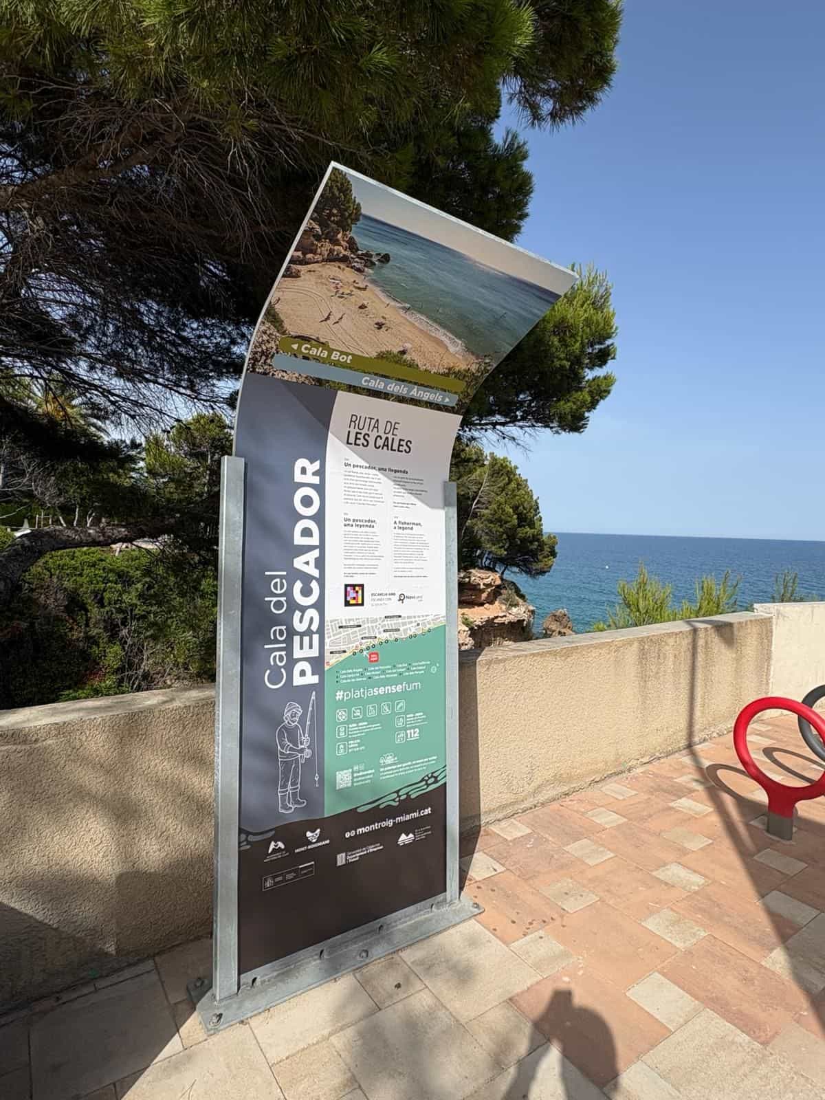 Nahaufnahme der Tafel an der Cala del Pescador: der Titel «RUTA DE LES CALES», die Geschichte «Un pescador, una llegenda» auf Katalanisch, Spanisch und Englisch, darunter der NaviLens-Code neben dem Hinweis «ESCANEJA AMB · ESCANEA CON · SCAN WITH» und dem NaviLens-GO-Logo