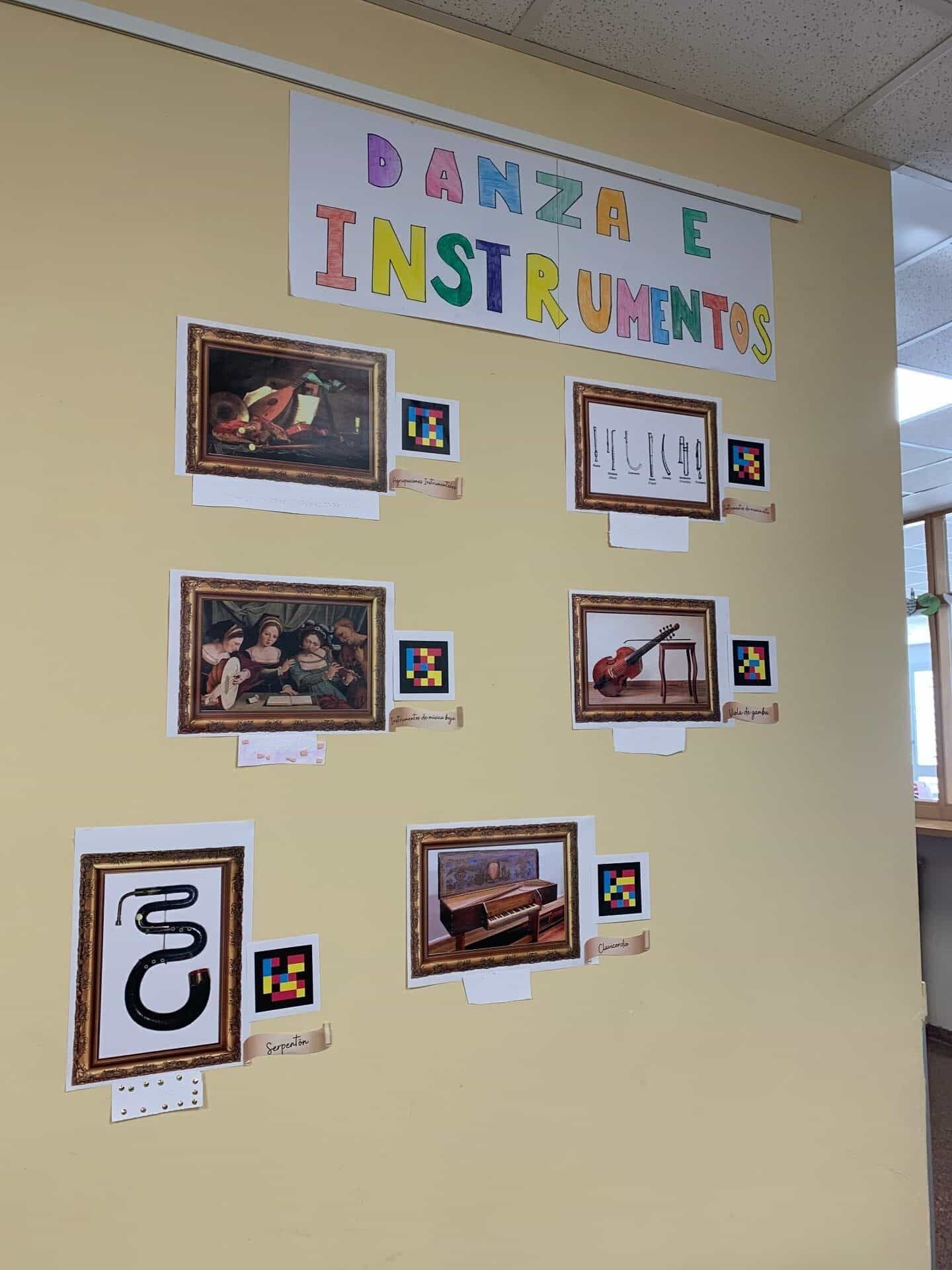 Tafel „Tanz und Instrumente“ mit sechs gerahmten Bildern – Instrumentalgruppen, hohe und tiefe Musikinstrumente, Viola da Gamba, Serpent und Clavichord – jeweils mit NaviLens-Code und Beschriftung, im Museum des IES Clara Campoamor