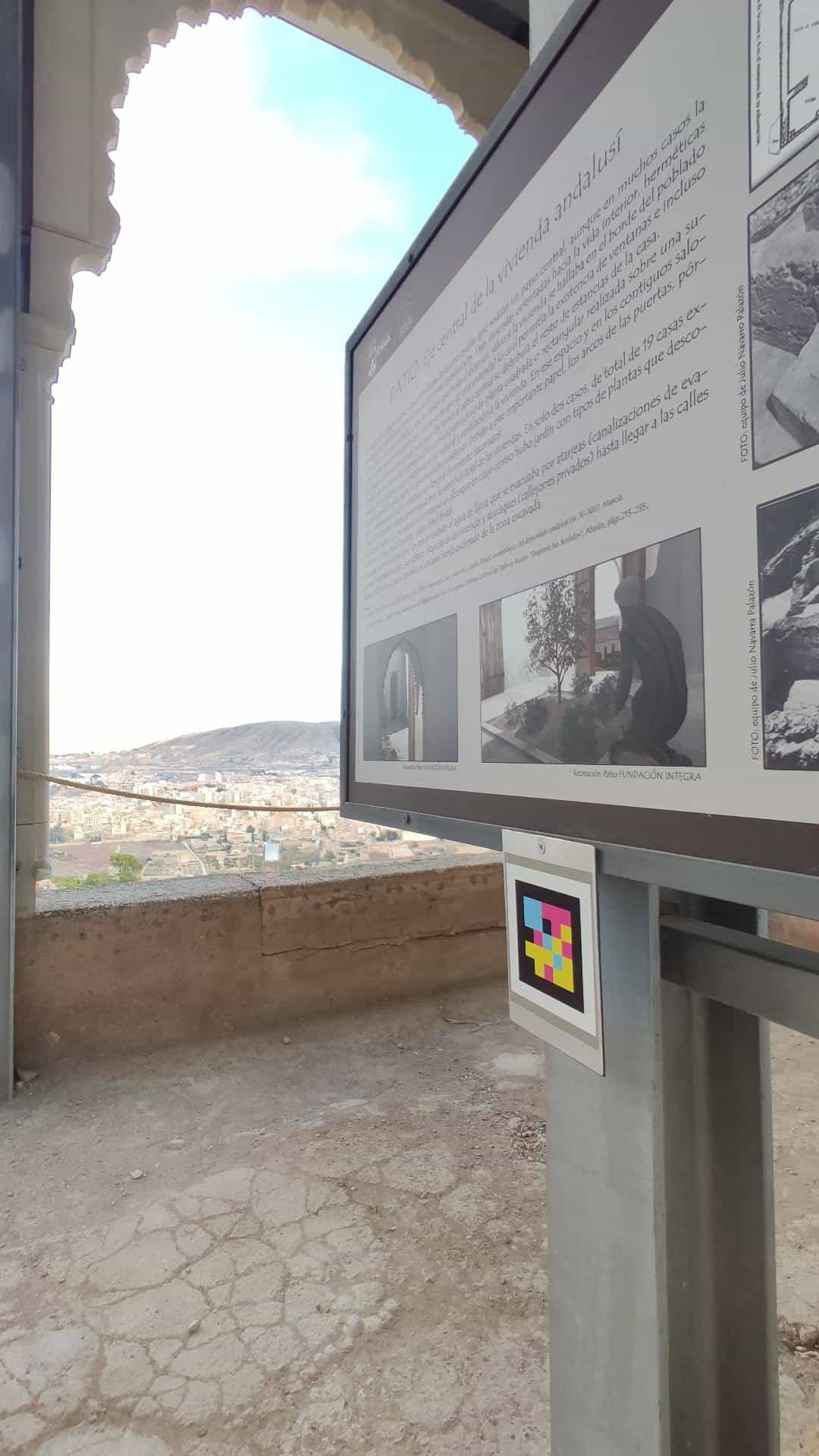 «Patio · eje central de la vivienda andalusí» panel at the Medina Siyâsa beside a restored multifoil arch, with a NaviLens code on the post