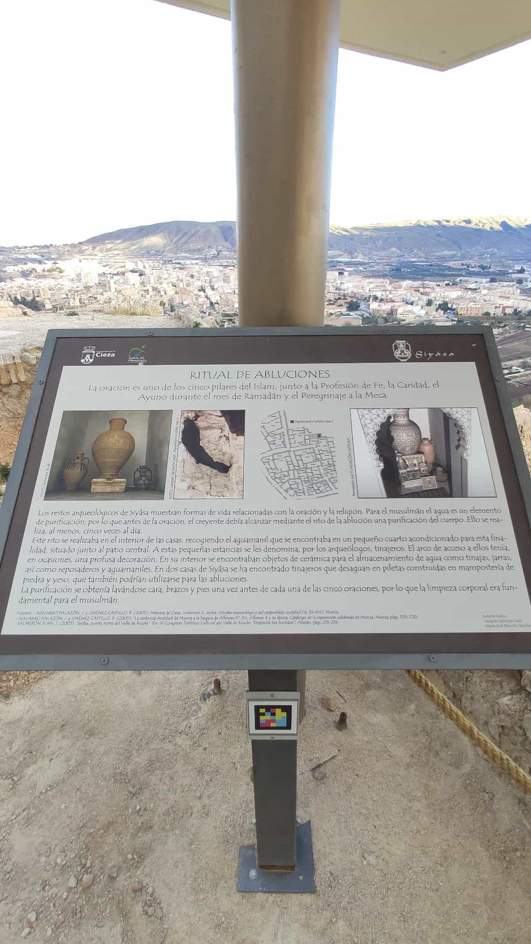 Panel «Ritual de abluciones» de la Medina Siyâsa con código NaviLens en el poste y vista panorámica de Cieza al fondo