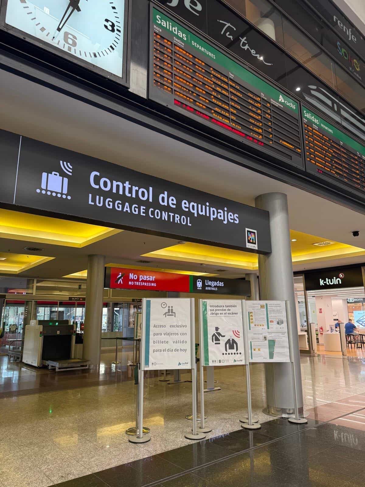 Estación de Málaga María Zambrano con paneles de salidas sobre el área de control de equipajes y un código NaviLens junto a la banda podotáctil del suelo
