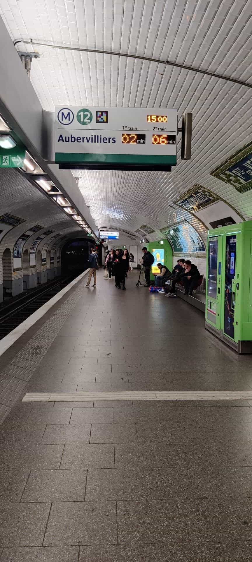 Panel de andén suspendido en Porte de Versailles con M12, dirección Aubervilliers y tiempos 02 min / 06 min, junto a un código NaviLens