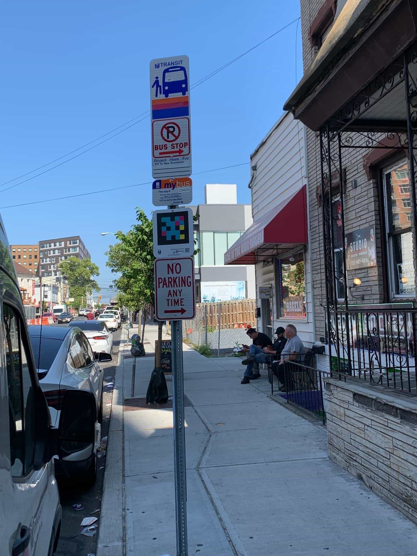 NJ TRANSIT-Schild mit mybus-Haltestelle Nr. 23429, NaviLens-Code und herunterladbarem QR, neben einem Bushaltestellen-/Parkverbotsschild an einer Straße in New Brunswick
