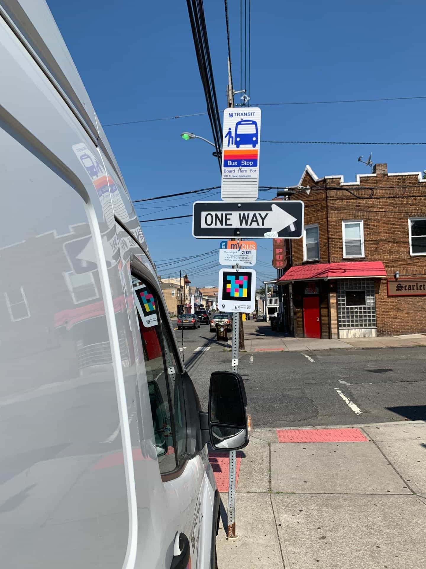 Ecke mit einem NJ TRANSIT-Schild, Einbahnstraßenschild und NaviLens-Code unter dem mybus-Schild Nr. 23430, vor einem Pub in New Brunswick