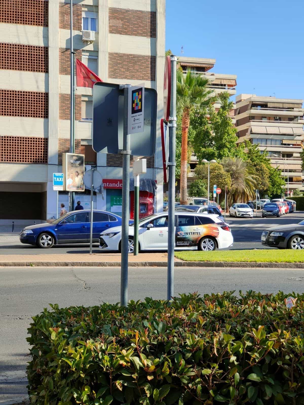Parada de taxi en una rotonda de Córdoba con cartel NaviLens y un taxi blanco al fondo