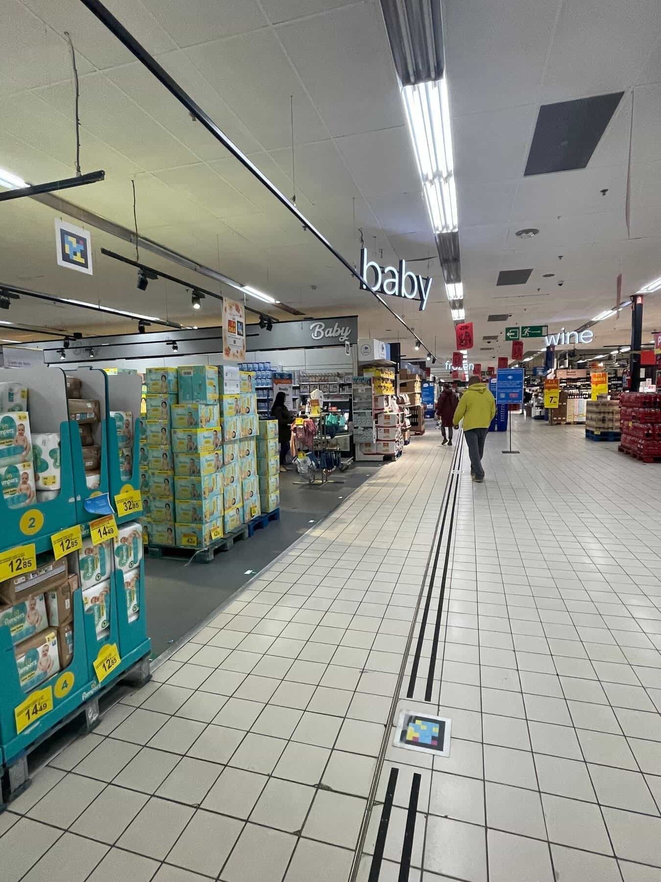 Babyabteilung im Carrefour Auderghem mit NaviLens-Code am Kopfende und einem weiteren auf dem Boden auf der taktilen Führungslinie