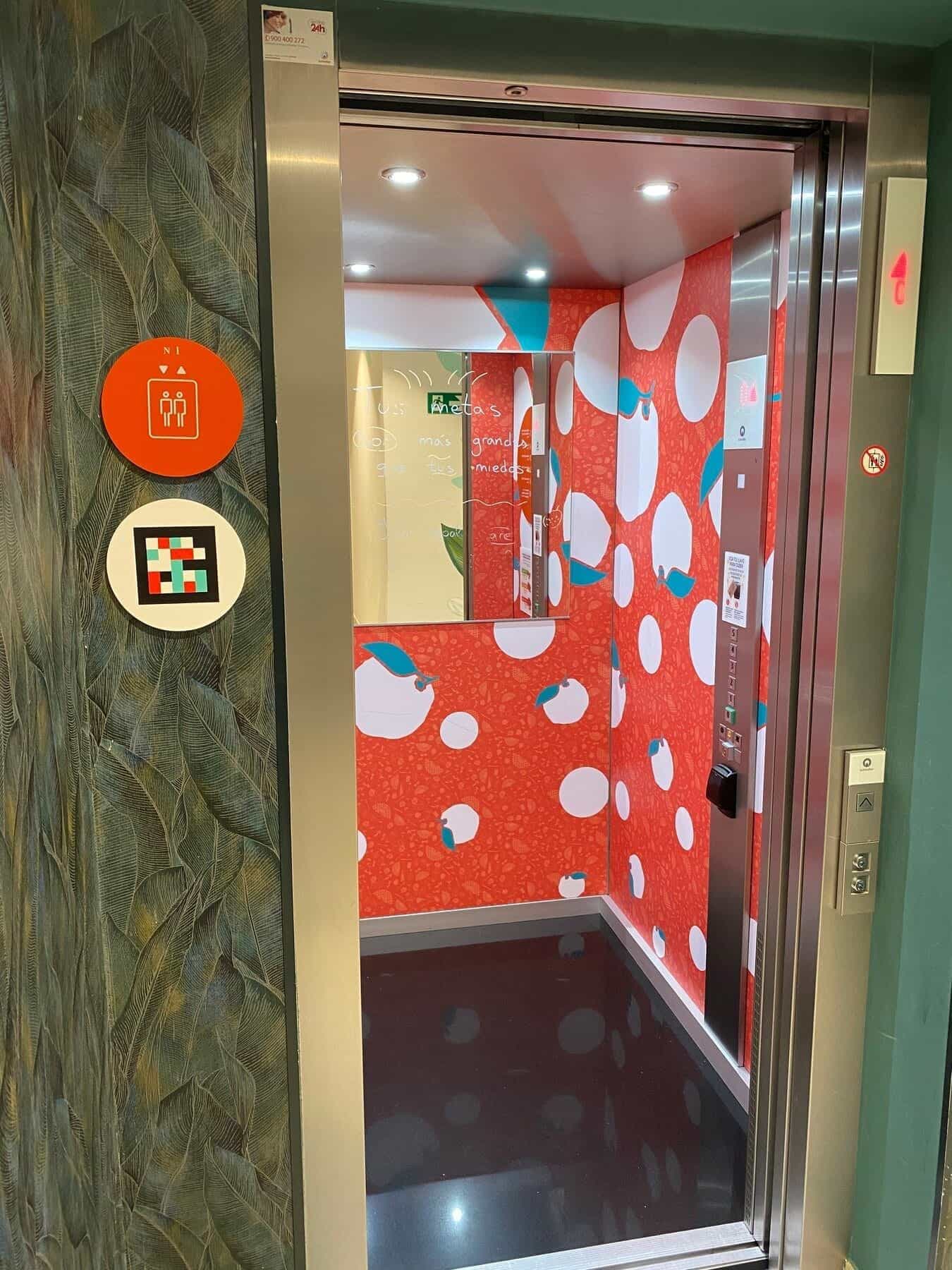 Langer Flur am ibis Styles Sevilla vom Geschoss aus: grüne Wand mit rundem Spiegel, orange gepunkteter Teppich und im Vordergrund der Türrahmen von Zimmer 63