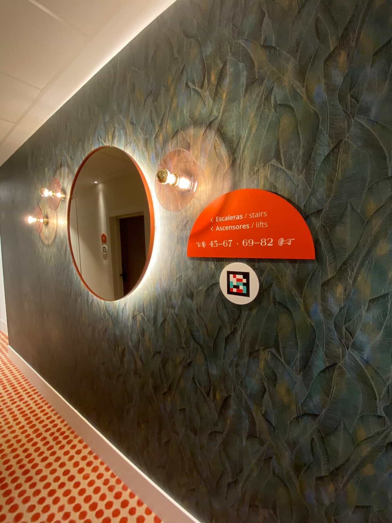 Flur am ibis Styles Sevilla perspektivisch: Zimmer 60 und 61 gegenüberliegend, jeweils mit rotem Nummern-Disc und NaviLens-Code am Türrahmen