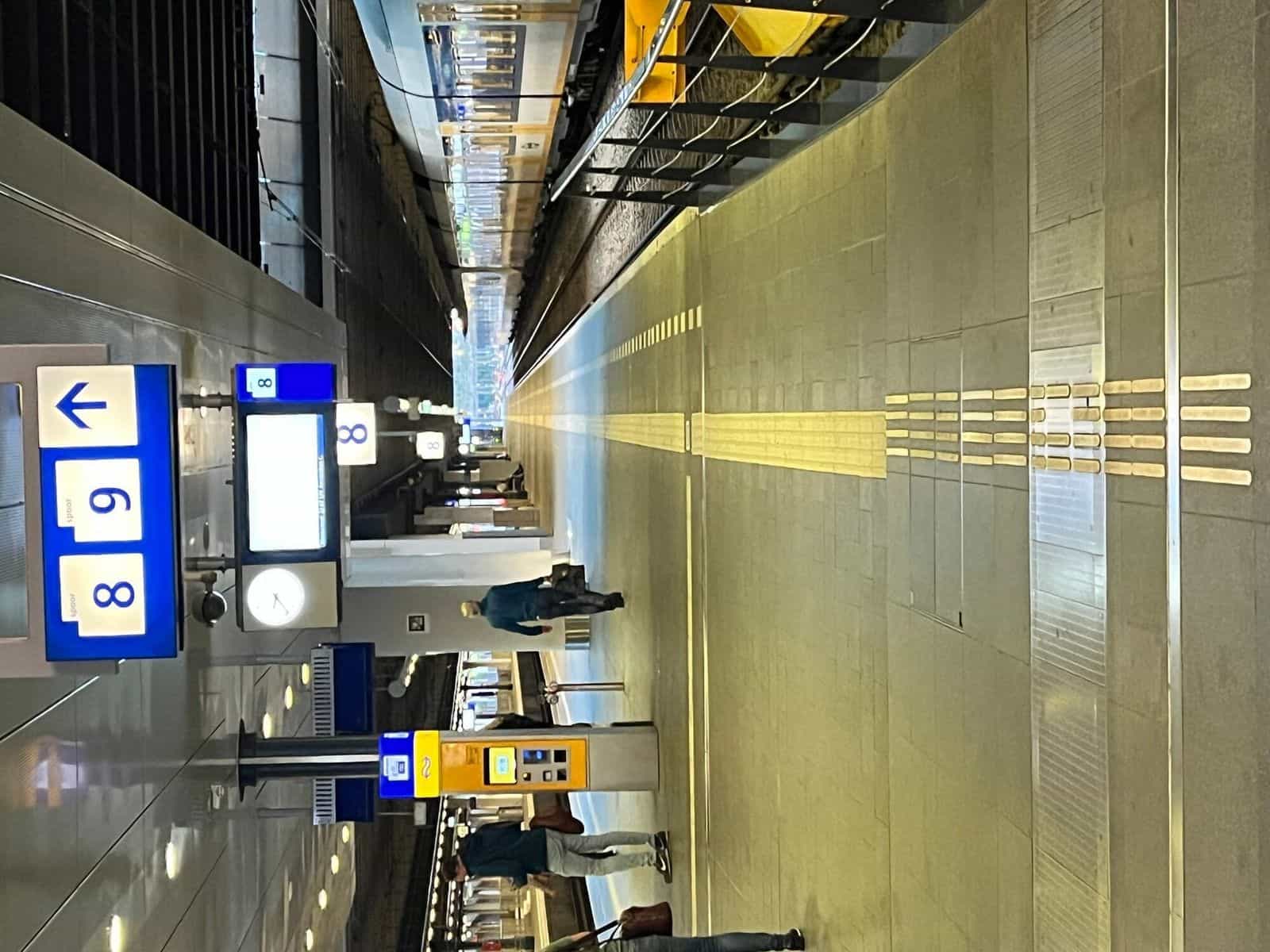 Banchina 8/9 di Den Haag Centraal con cartello azzurro del binario, macchina gialla NS e linea guida tattile a doppia fascia che percorre tutta la lunghezza della banchina