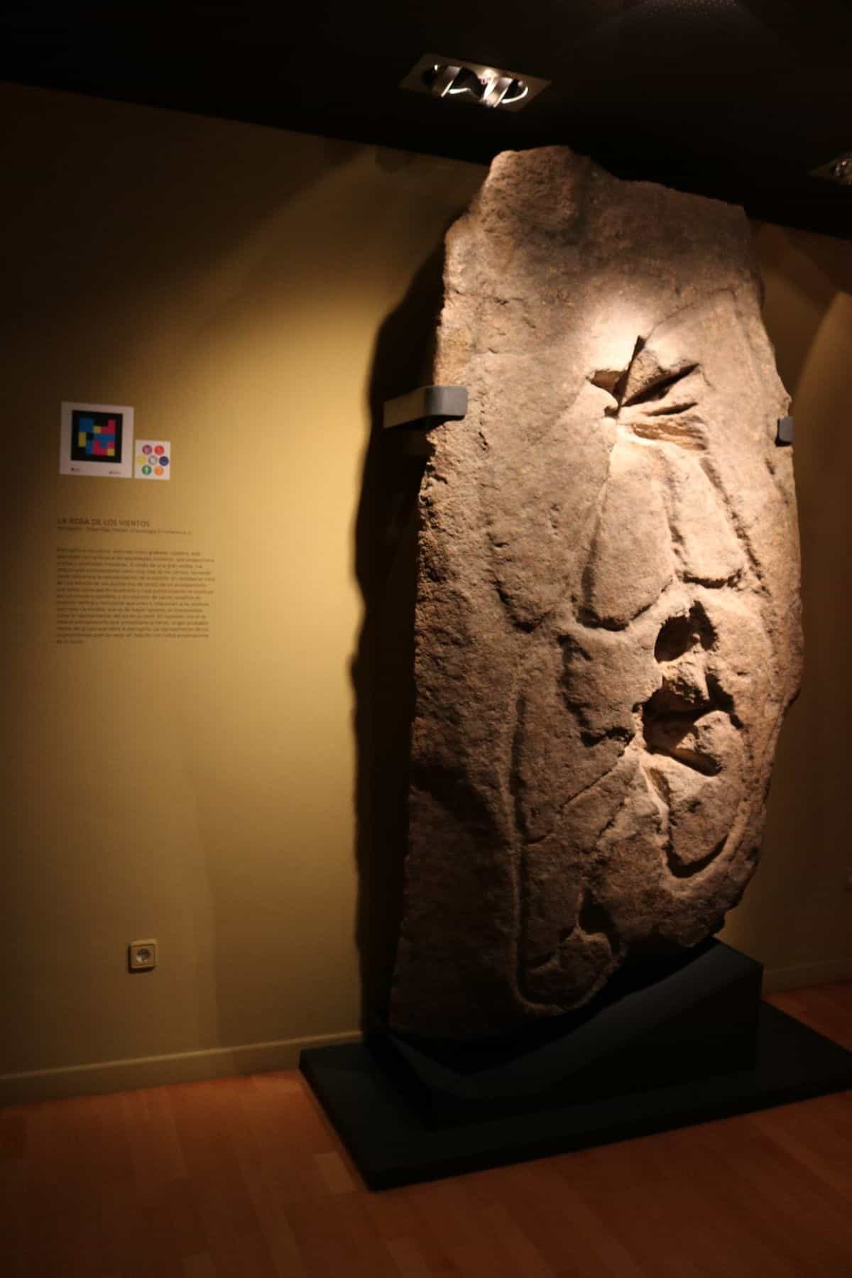 Petroglyph „La Rosa de los Vientos“ im Städtischen Archäologischen Museum Cayetano de Mergelina in Yecla, mit Erklärungstafel und NaviLens-Code an der Seitenwand
