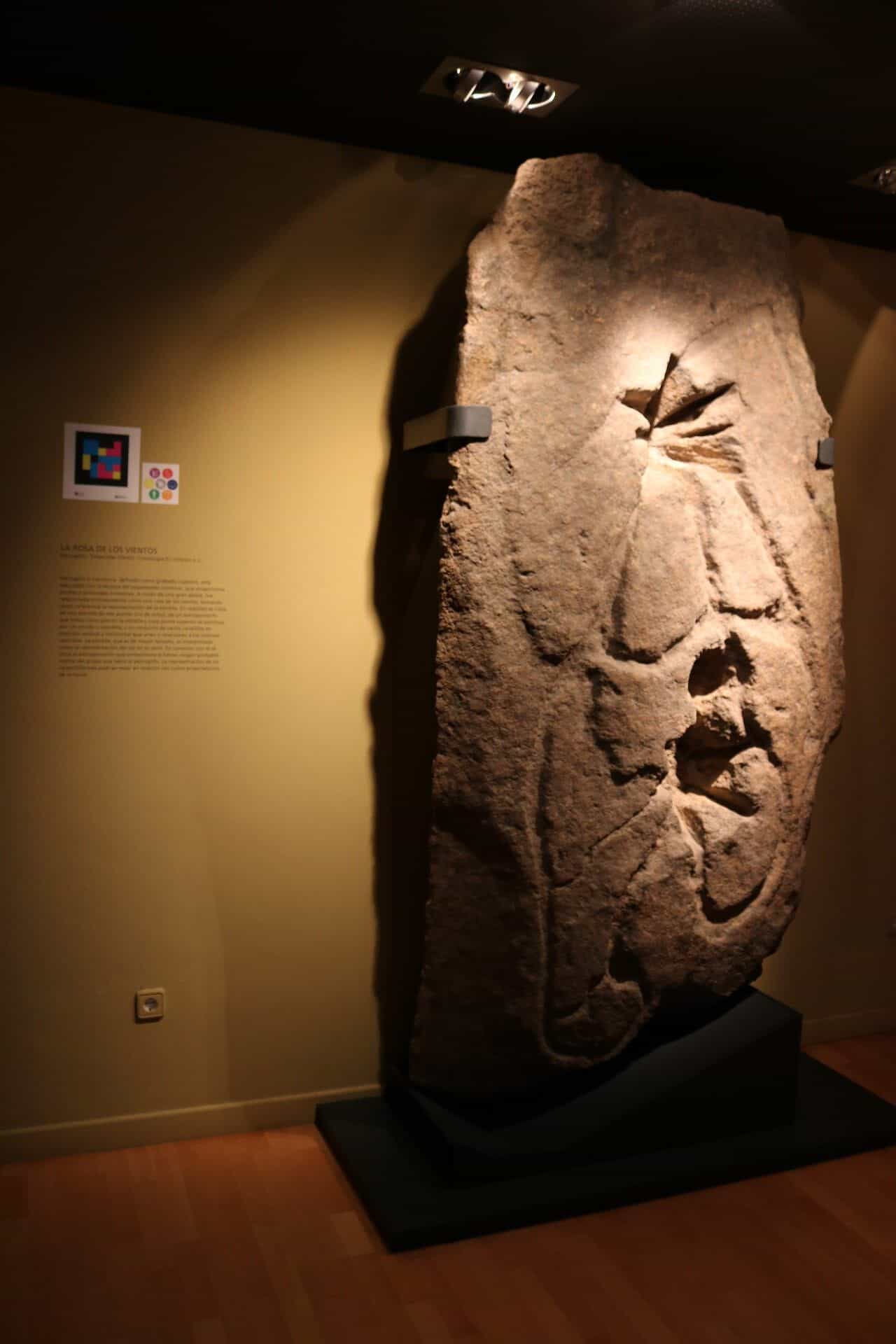 Petroglyph „La Rosa de los Vientos“ im Städtischen Archäologischen Museum Cayetano de Mergelina in Yecla, mit Erklärungstafel und NaviLens-Code an der Seitenwand