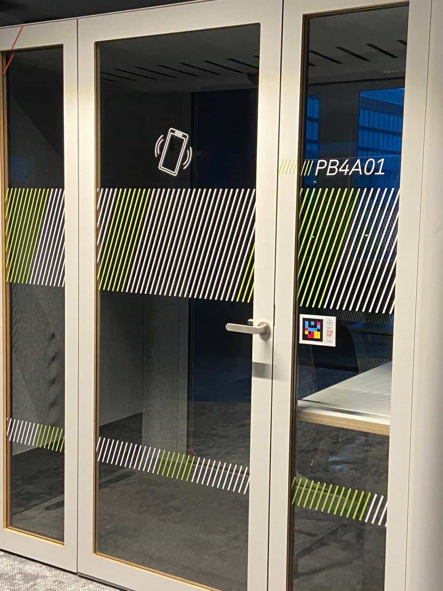 Phone booth PB4A01 at Bayer's Leverkusen HQ — NaviLens sign with Bayer cross on the glass door, next to the mobile-phone pictogram and the booth's oblique signage