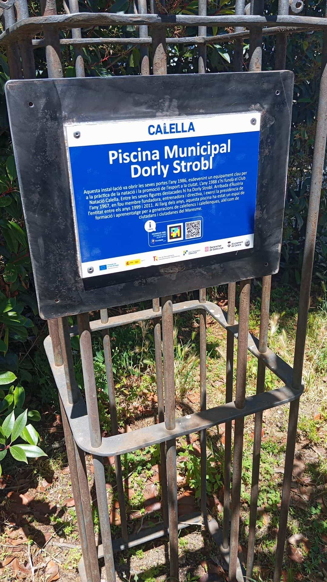 Placa azul de la Piscina Municipal Dorly Strobl de Calella con código NaviLens instalada en la valla del equipamiento