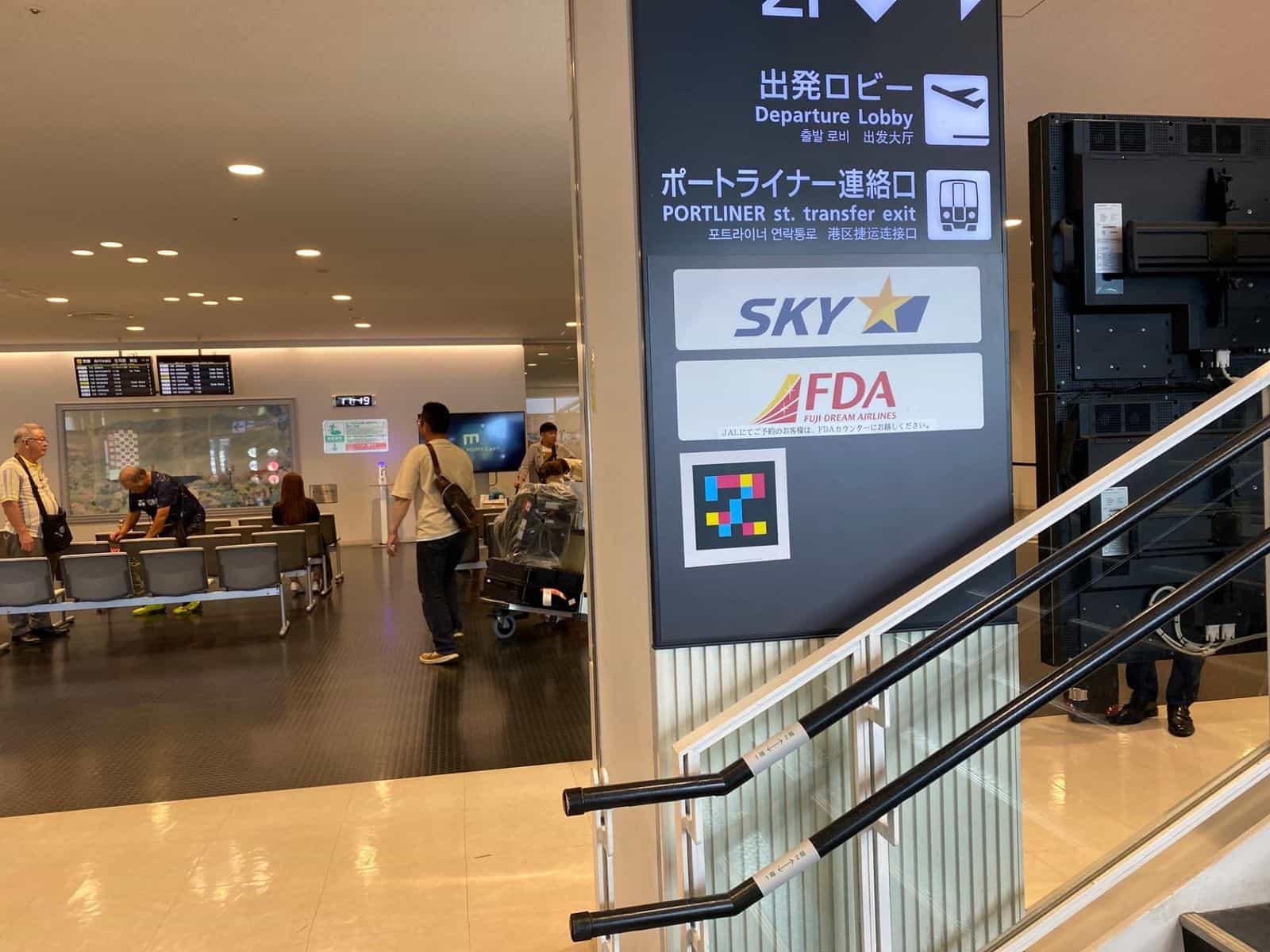 Dunkelblaues Hängeschild im Kobe Airport mit «Departure Lobby» und «PORTLINER st. transfer exit», SKY- und FDA-Logos und NaviLens-GO-Tag