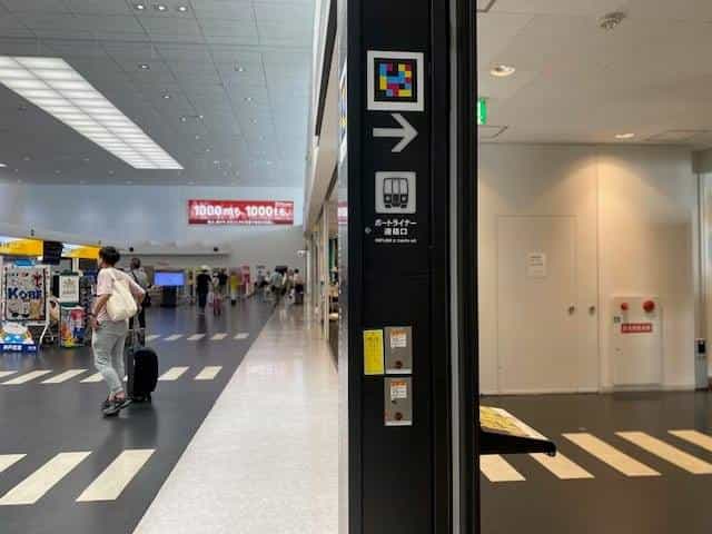 Black pillar in the Kobe Airport hall with NaviLens tag, right-pointing arrow and train pictogram under “PORTLINER st. transfer exit”