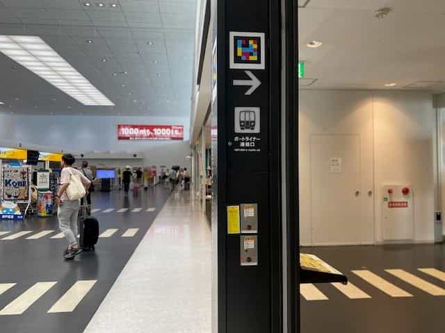 Schwarzer Pfeiler in der Halle des Kobe Airport mit NaviLens-Tag, Pfeil nach rechts und Zug-Piktogramm unter «PORTLINER st. transfer exit»