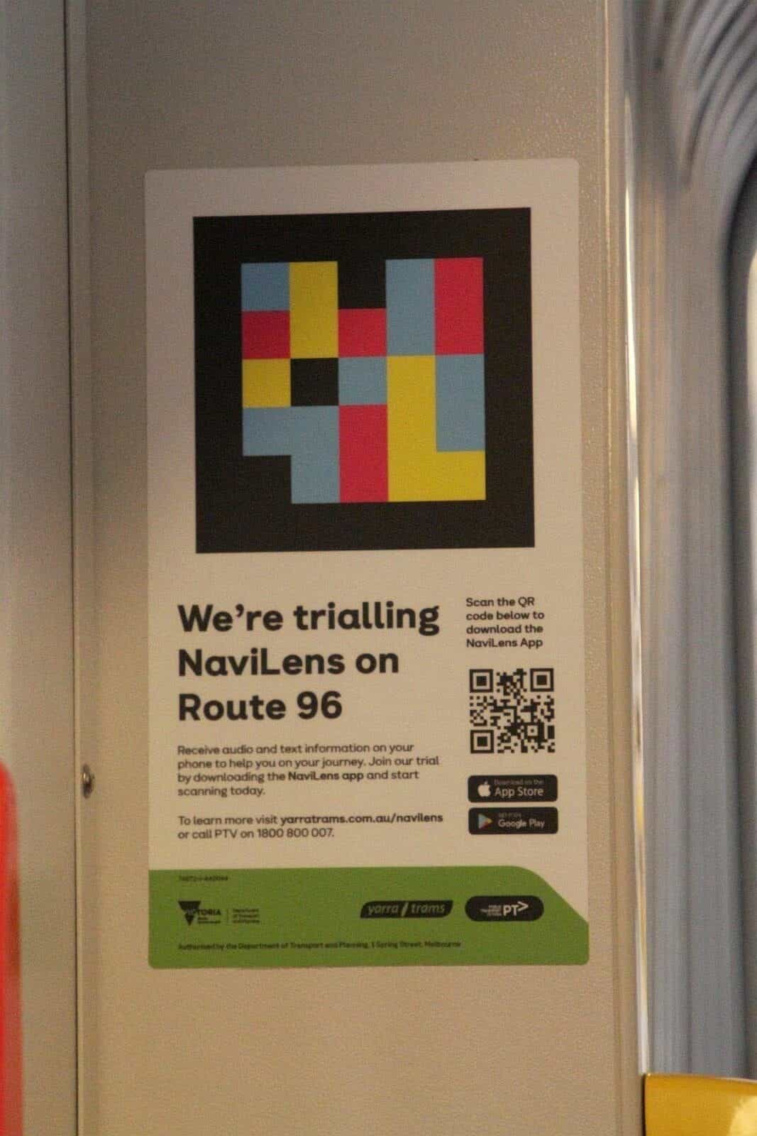 Póster interior dentro de un tranvía de Yarra Trams con un código NaviLens reproducido a gran tamaño en su parte superior y, debajo, el texto «We’re trialling NaviLens on Route 96» y un QR para descargar la app, junto a los logos verdes de Victoria, Yarra Trams y PTV