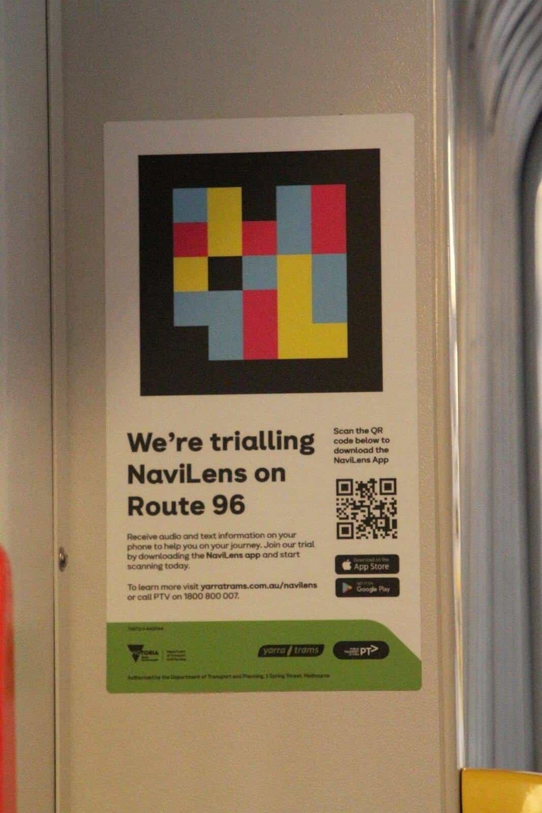 Interior poster inside a Yarra Trams tram with a NaviLens code reproduced at large size at the top and, below, the text “We’re trialling NaviLens on Route 96” and a QR code to download the app, next to the green Victoria, Yarra Trams and PTV logos