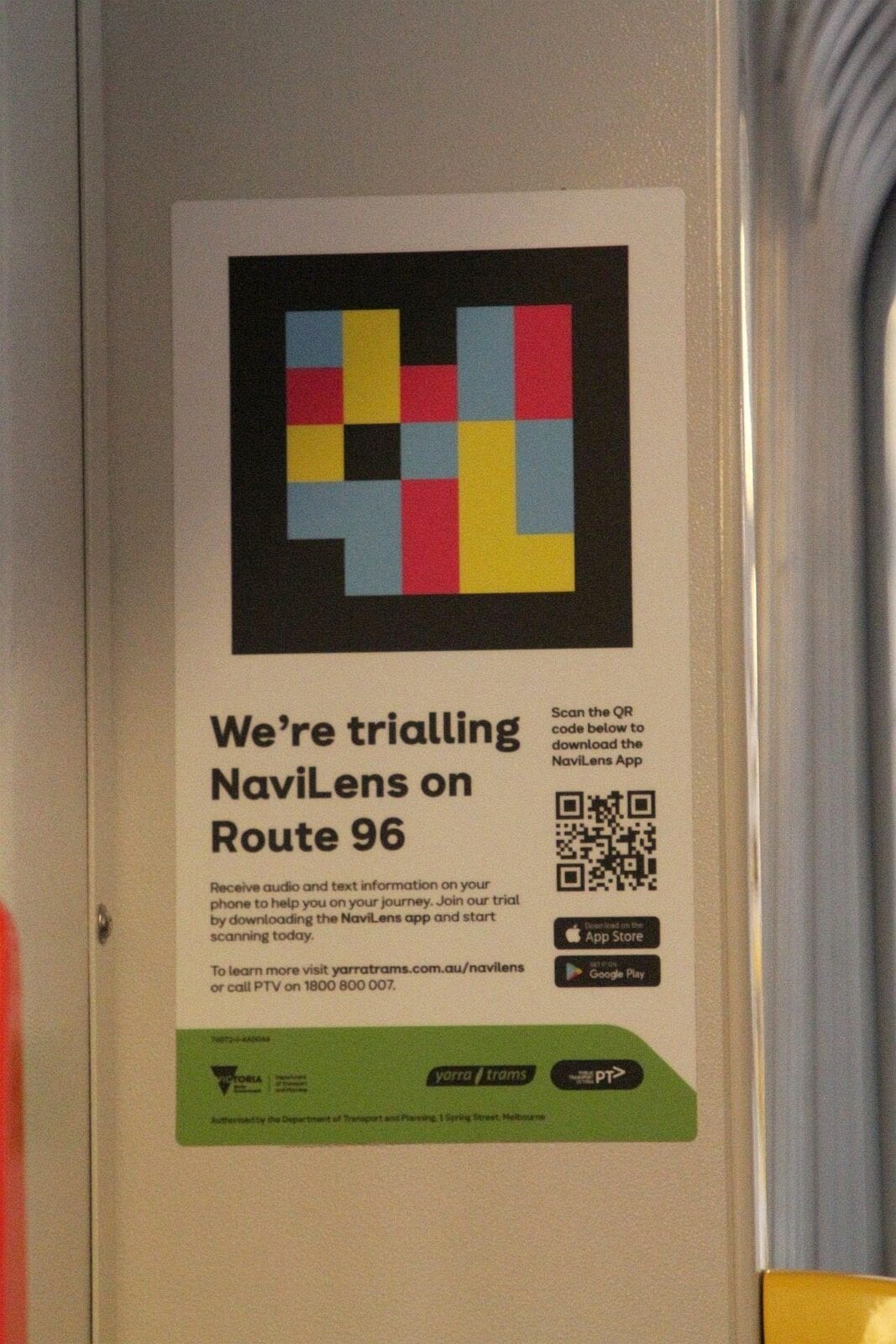 Interior poster inside a Yarra Trams tram with a NaviLens code reproduced at large size at the top and, below, the text «We’re trialling NaviLens on Route 96» and a QR code to download the app, next to the green Victoria, Yarra Trams and PTV logos