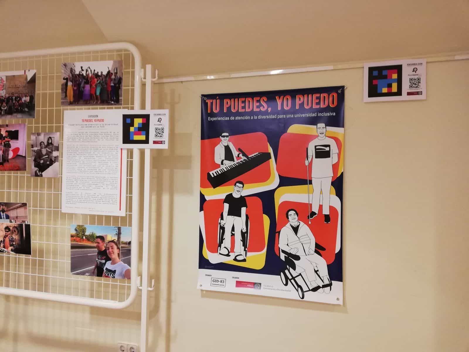 Blick auf die Ausstellung „Tú puedes, yo puedo“ in einem Flur der Fakultät für Kommunikation und Dokumentation der UMU: offizielles Plakat mit vier illustrierten Porträts und darüber eine weiße Karte mit NaviLens-Code und dem Hinweis „MIT NaviLensGO SCANNEN“
