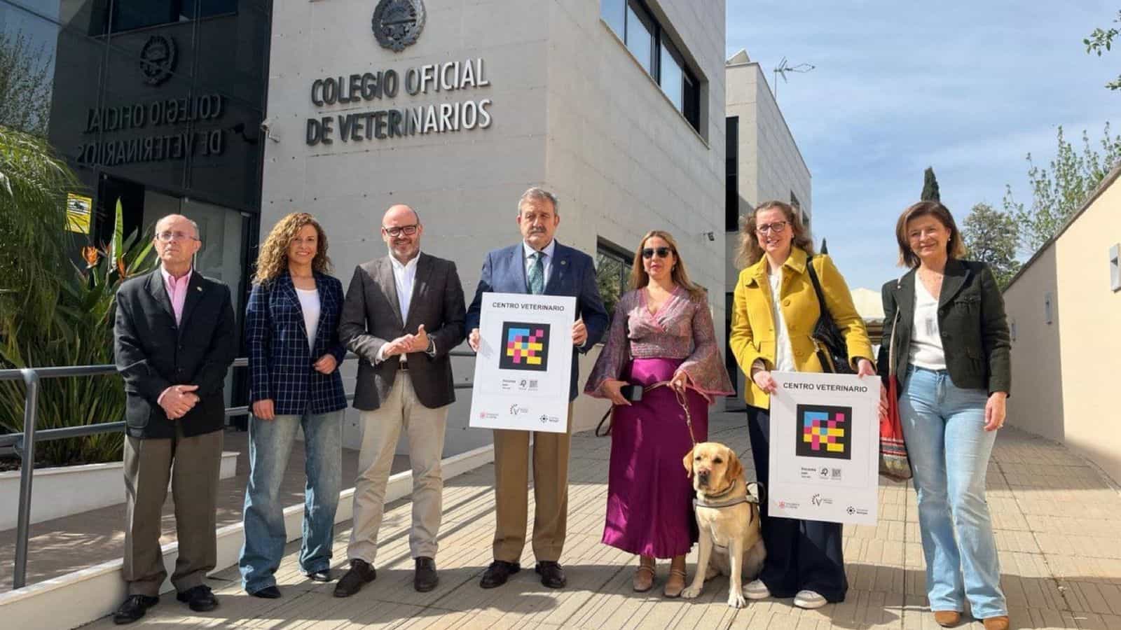 Launch of the «Centros Veterinarios Accesibles y Cercanos» project outside the Colegio Oficial de Veterinarios de Córdoba: institutional representatives, a user with a guide dog and two «Centro Veterinario» stickers carrying a NaviLens code