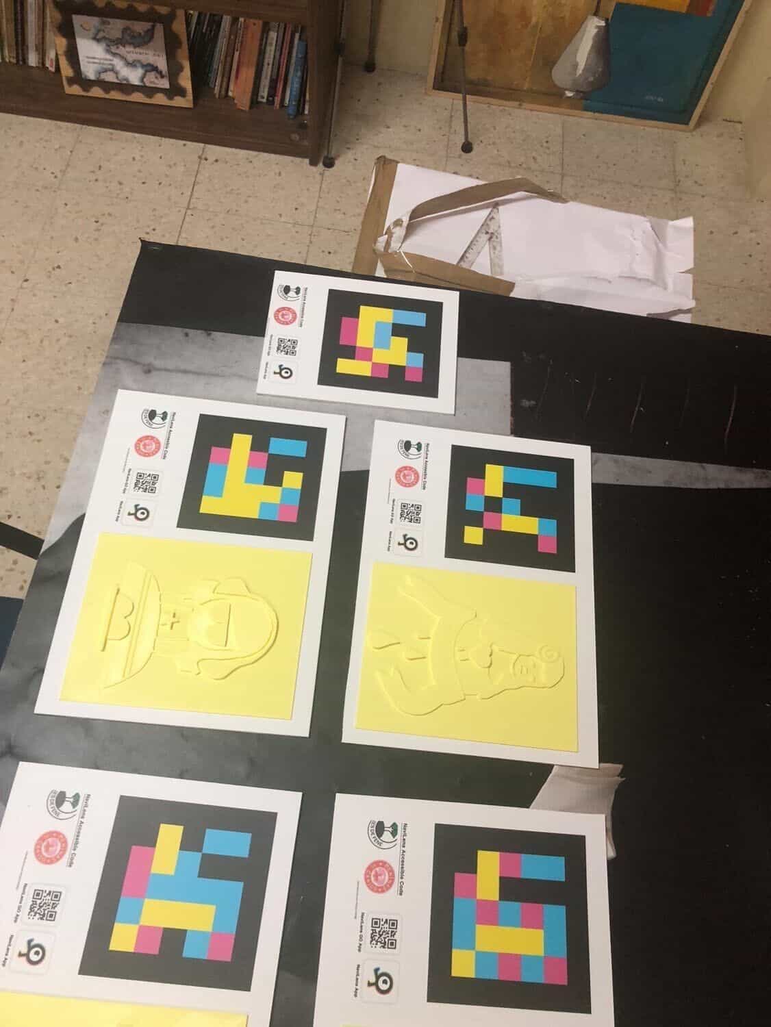 Varios paneles «Tocando as Meninas» dispuestos sobre el suelo del taller del IES de Fene: códigos NaviLens y relieves amarillos en 3D listos para instalar