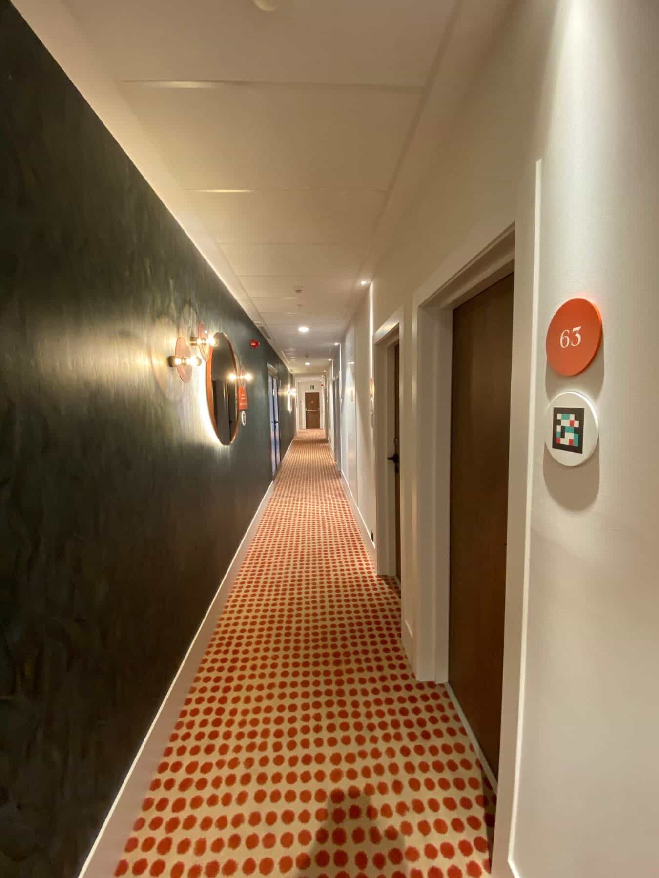 Tür eines barrierefreien Zimmers am ibis Styles Sevilla mit Doppelnummer „80 / 82“ auf rotem Disc und NaviLens-Code auf weißem Disc; Holztür mit elektronischem Schloss