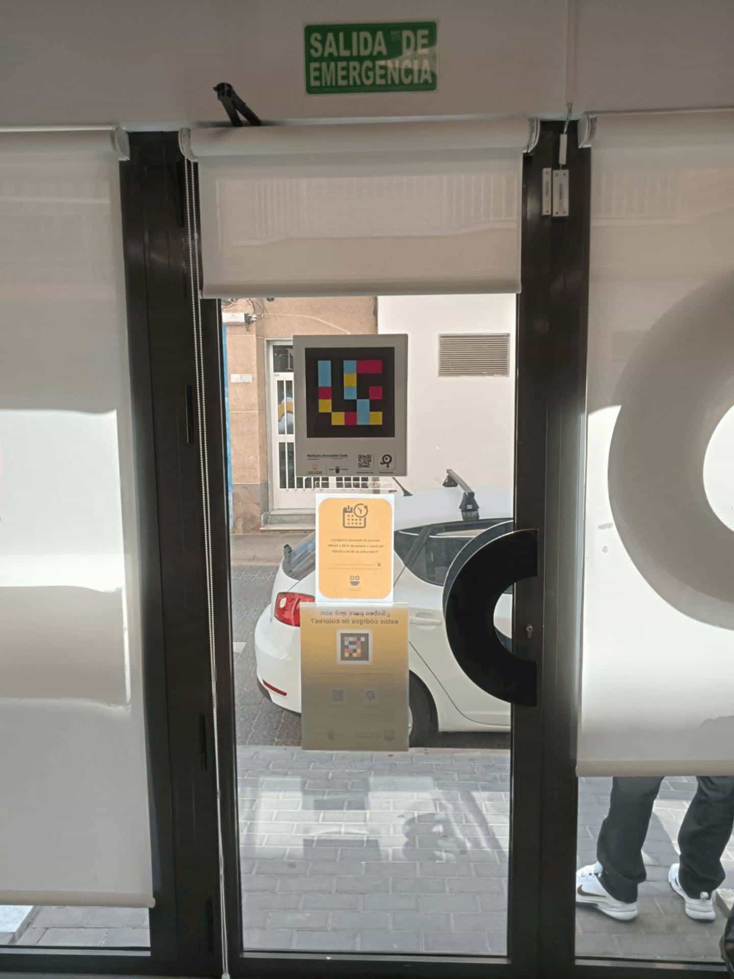 Same door seen from inside: green “EMERGENCY EXIT” sign, NaviLens code, opening hours and leaflet mirrored, with ATRM logo in matte white vinyl.