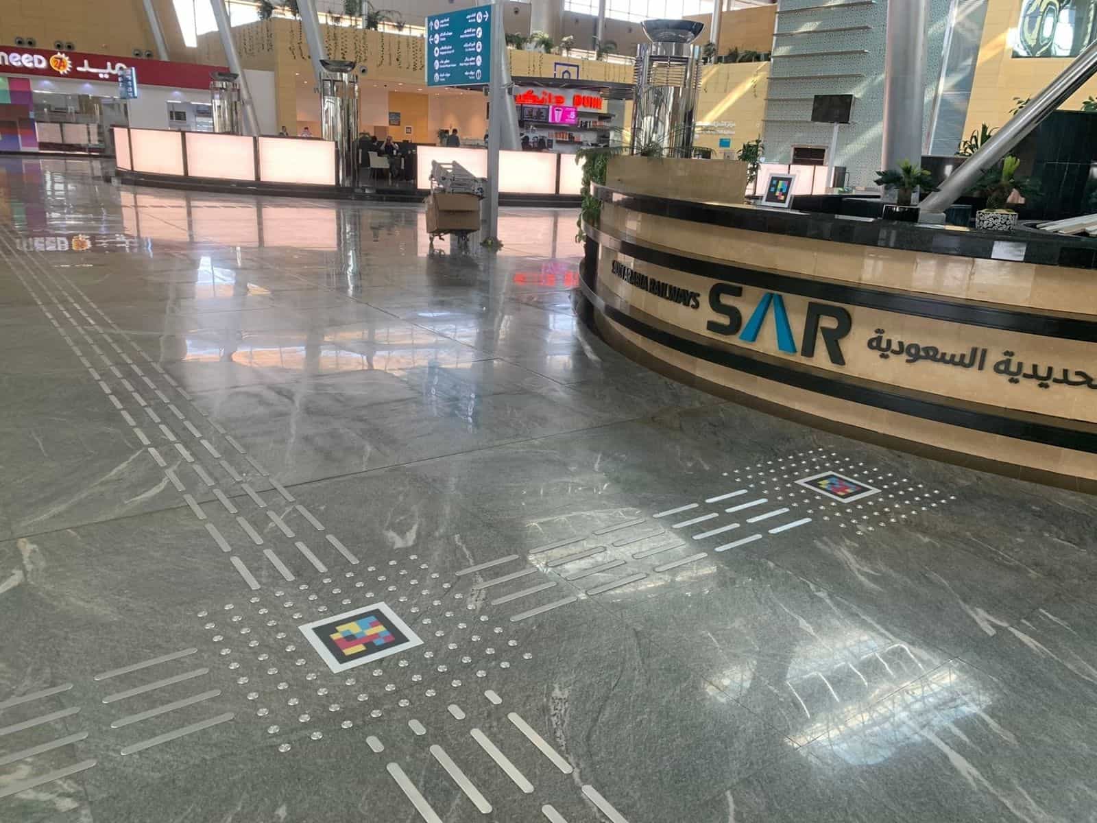 リヤド駅にある曲線状の「Saudi Arabia Railways SAR」カウンター。カウンター上のNaviLensコードと、点字ブロックが横切る大理石の床に埋め込まれたもう一つのコード