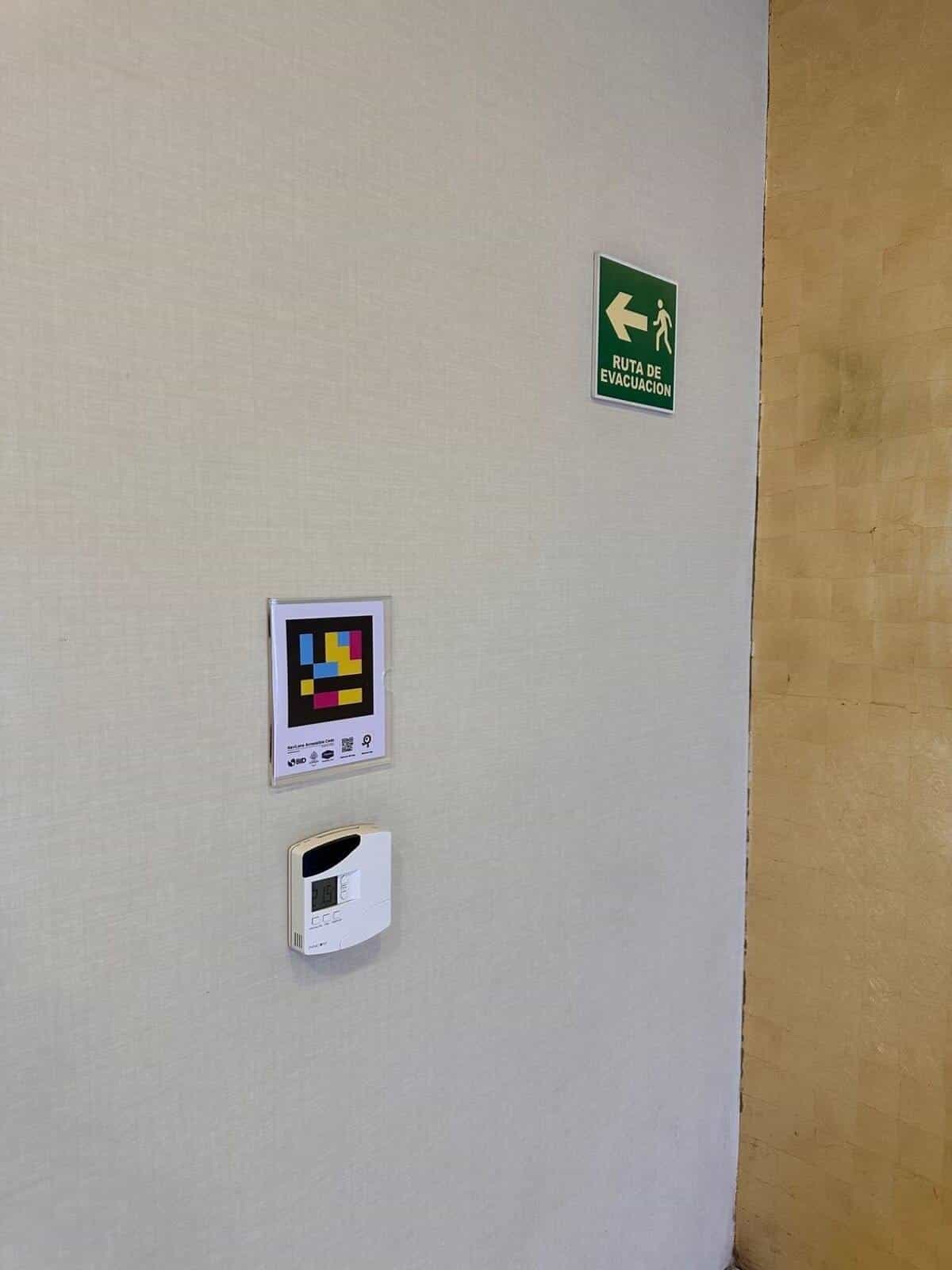 NaviLens sign on the interior wall next to the green “Evacuation route” sign and the corridor thermostat