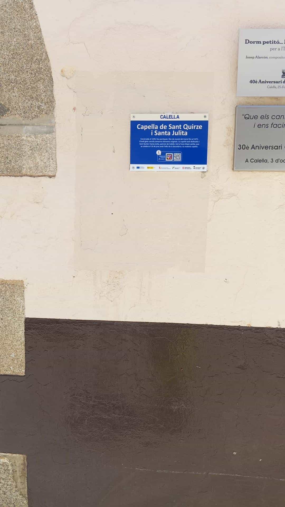 Blue CALELLA plaque of the Chapel of Sant Quirze i Santa Julita with a NaviLens code, mounted on the façade