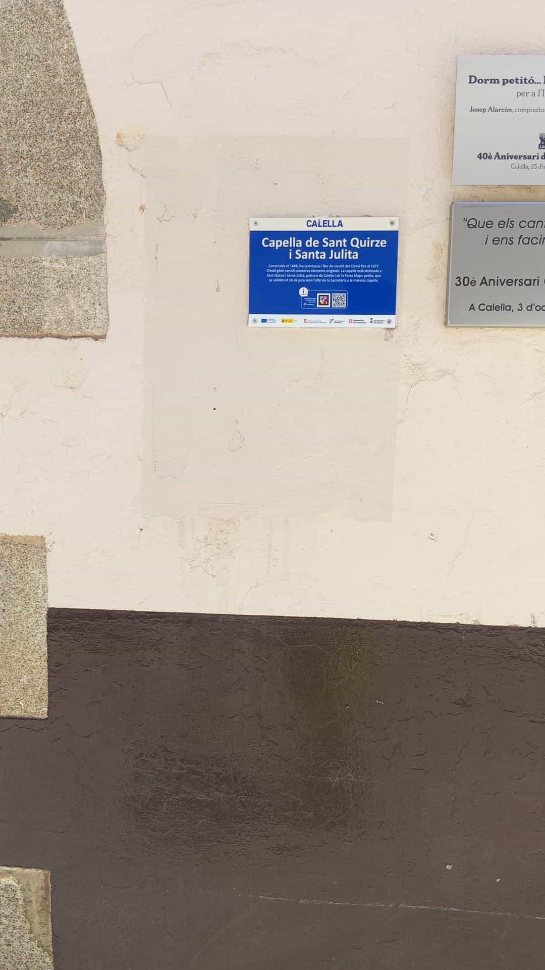 Placa azul CALELLA de la Capella de Sant Quirze i Santa Julita con código NaviLens en la fachada