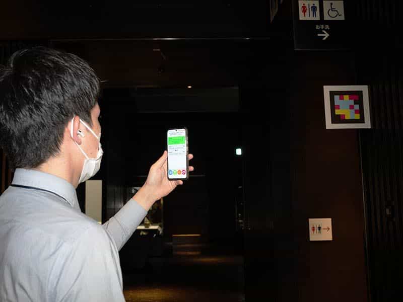 博物館のお手洗いのサインの横に設置されたNaviLensコードに、来館者がスマートフォンをかざしている様子
