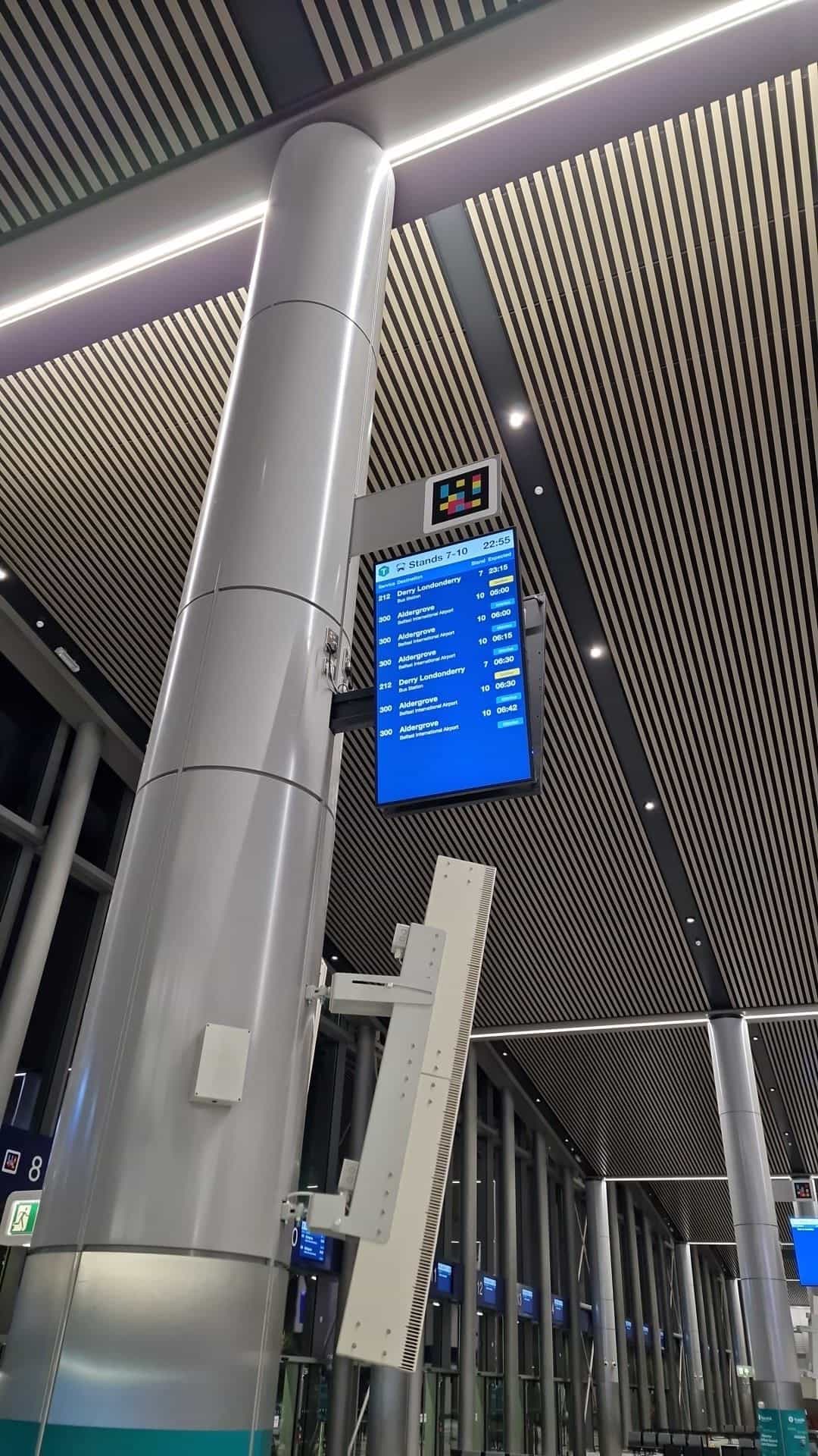 Überkopfanzeige der Stände 7–10 in Belfast Grand Central mit NaviLens-Code und den Diensten 212 Derry Londonderry und 300 Aldergrove