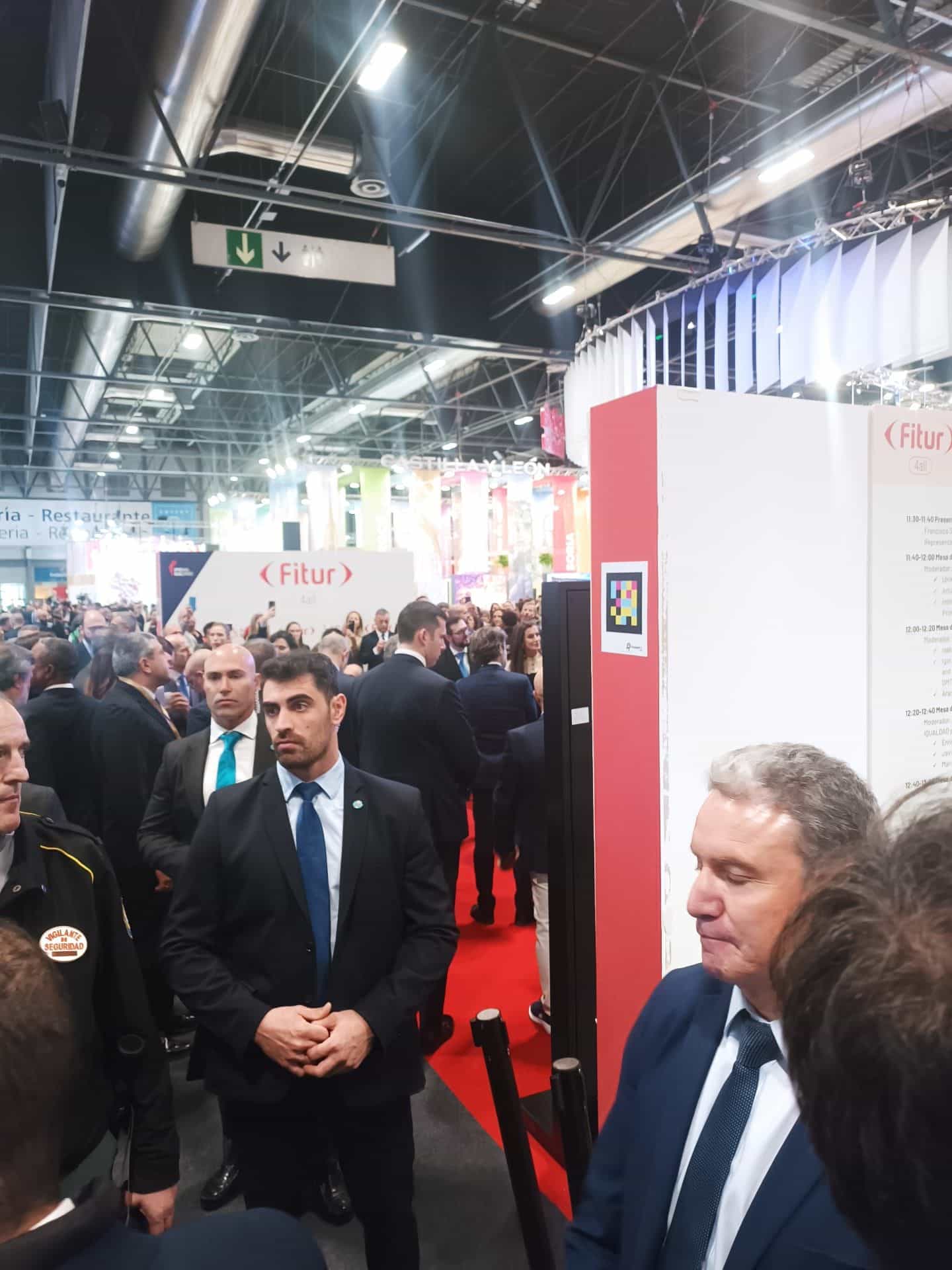 Stand di FITUR 4all a IFEMA MADRID durante l’inaugurazione: su una colonna dell’espositore in rosso e bianco con il logo «(Fitur) 4all», un codice NaviLens quadrato a colori accanto al programma delle giornate; in fondo, autorità e stampa percorrono il tappeto rosso
