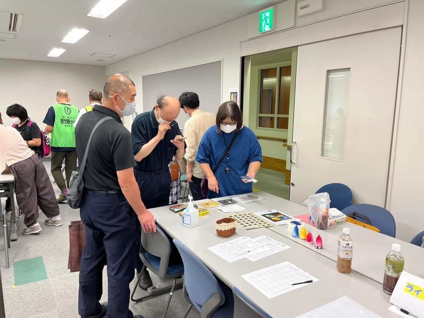 Mayudama Net Festa stand with several attendees consulting NaviLens codes on a table: green vest “視覚障害がい者”