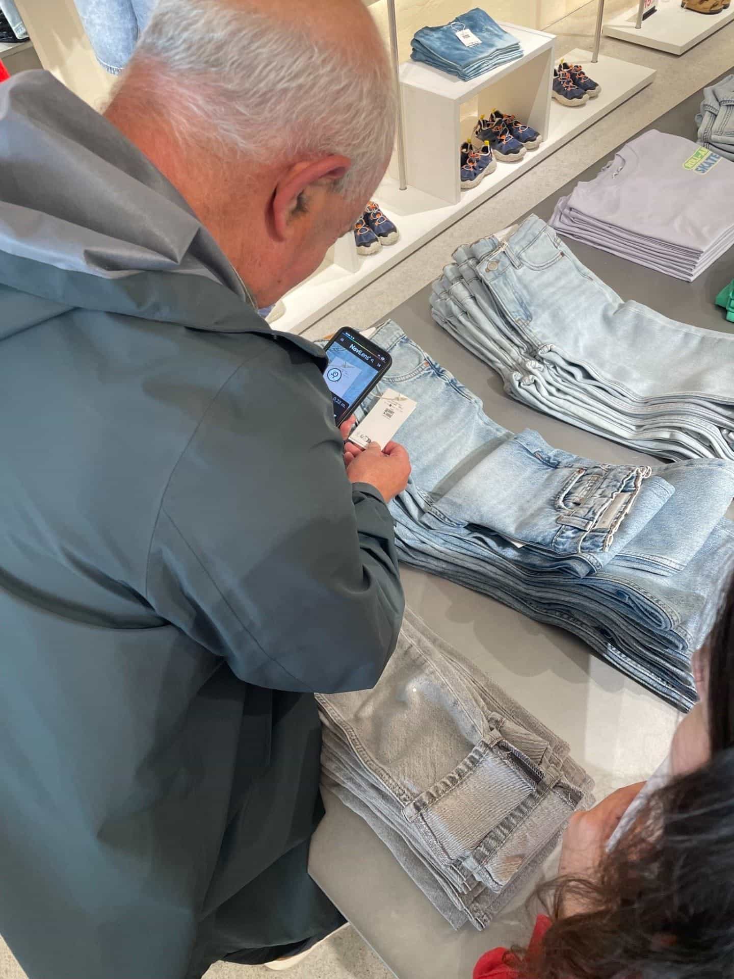 Cliente che scansiona da sopra la spalla il cartellino di un paio di jeans con l’app NaviLens all’interno di un negozio.