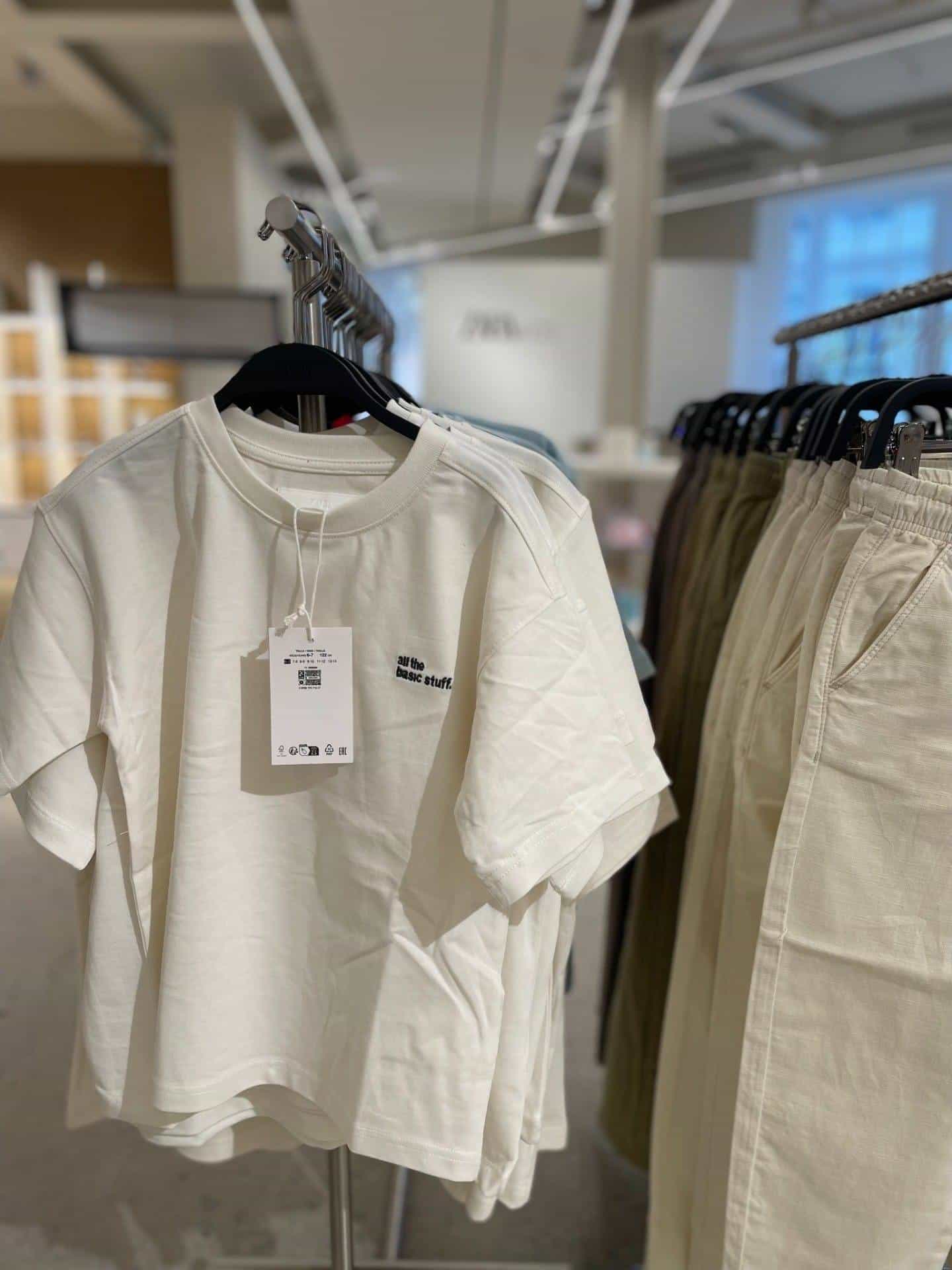 White t-shirt on a hanger in an Inditex store, with a hangtag showing a NaviLens code and size information.