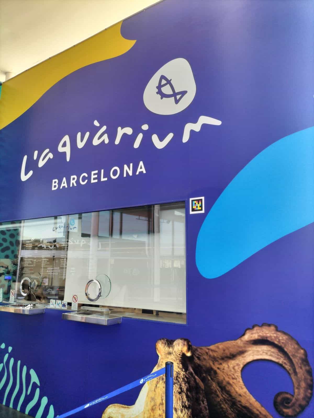 Fachada azul de L'Aquàrium de Barcelona con el logotipo y un código NaviLens junto a la taquilla de venta de entradas